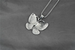 Detailed close-up of a silver butterfly pendant with brushed metal texture and box chain