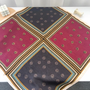 Close-up of square silk scarf with geometric red and charcoal patterns and gold leaf details