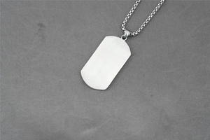 Close-up of brushed stainless steel rectangle pendant and round box chain on grey fabric