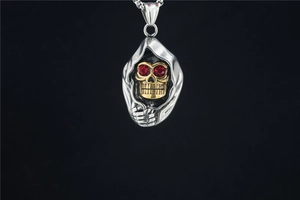 Détail du pendentif crâne de faucheuse gothique avec visage doré et yeux en gemmes rouges