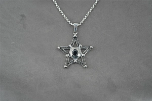 Macro detail of pentagram pendant with black onyx center on textured grey fabric