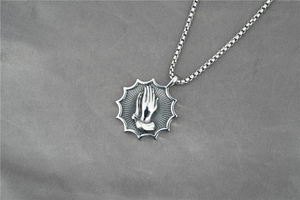 Gros plan du pendentif mains en prière rétro avec bordure solaire sur chaîne box fine