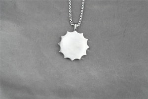 Détail d'un pendentif de prière vintage aux bords rayonnants et chaîne à maillons carrés