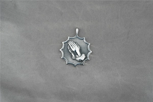 Détail macro du pendentif mains en prière vintage argenté avec texture soleil oxydée