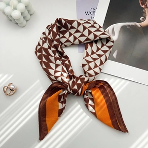 Dettaglio di un foulard effetto seta annodato a fiocco con motivi geometrici e bordi marroni