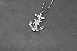 Detailed view of silver pirate anchor pendant with box chain on dark textured fabric