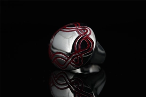 Close-up of red enamel patterns on irregular stainless steel ring with reflections
