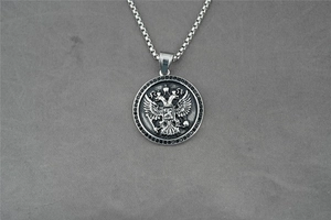 Détail du pendentif aigle à deux têtes argenté avec zircons noirs sur tissu gris