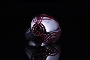 Detail of silver stainless steel ring with red Celtic knot enamel patterns on black surface