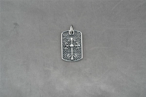 Detaillierte Makroansicht von Vintage-Silberkreuz und Lilienmuster auf quadratischem Anhänger