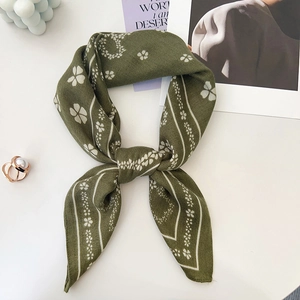 Detailed macro view of olive green floral square scarf knotted on a minimal white surface