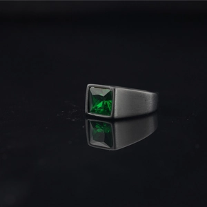 Matte black stainless steel ring with emerald green square zircon on a reflective surface