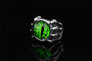 Detailed close-up of a silver dragon claw ring with a green evil eye stone on black mirror