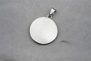 Détail d'un pendentif rond argenté brossé mat avec bélière triangulaire sur tissu