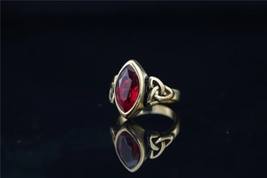 Détail d'une bague vintage en acier doré avec pierre marquise rouge et motif nœud celte