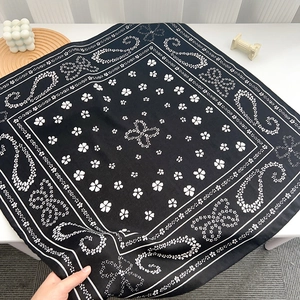Detail of soft black square scarf with white paisley patterns held to show drape texture