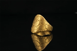 Macro detail of gold tone punk rock ring featuring unique pebble texture on black background