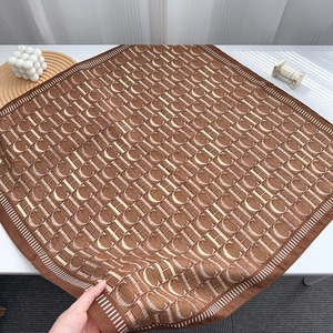 Macro detail of brown pleated silk scarf with white monogram patterns and soft texture