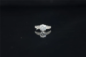 Macro view of round cut moissanite ring with pavé side stones on a reflective surface