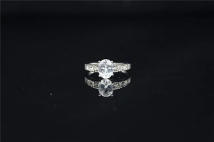Macro view of a classic oval moissanite ring with side stones on a reflective black background