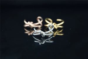 Dettaglio di anelli a nodo minimalisti in argento, oro e oro rosa su sfondo scuro