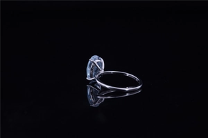 Macro detail of oval blue gemstone ring with four-prong silver setting on black surface