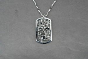 Close-up of square metal pendant featuring a detailed crucifix with grainy texture background