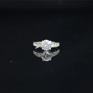Classic moissanite engagement ring with round center stone and pave band on black reflection