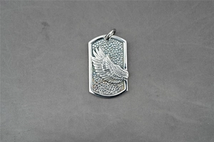 Detailed close-up of silver military dog tag pendant with embossed wing and feather patterns