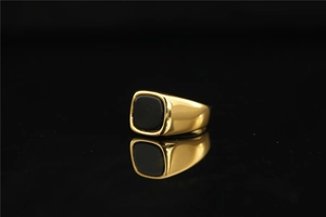 Gros plan d'une bague dorée avec pierre précieuse noire et reflet sur surface lisse