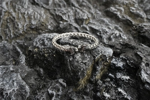 Macro detail of silver braided twist bracelet with tiger head sculpture on dark rock
