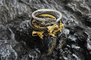 Macro detail of braided steel cable bracelets featuring intricate dragon heads on dark rock