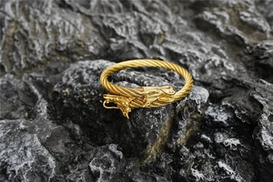 Detail of a golden braided stainless steel cable bracelet featuring dual dragon heads