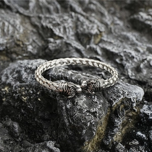 Vintage braided titanium steel bangle with double tiger heads on dark rock background