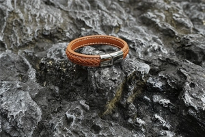 Detail eines braunen Lederarmbands mit Magnetverschluss aus Silber auf dunklem Stein