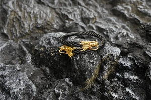 Macro detail of braided black steel cable bracelet with gold dragon heads and red eyes