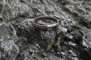 Detail eines braunen Lederarmbands mit silbernem Magnetverschluss auf einer Steinfläche