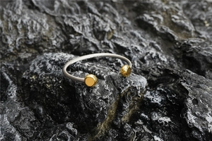 Gros plan du bracelet jonc torsadé avec extrémités à billes dorées sur pierre sombre