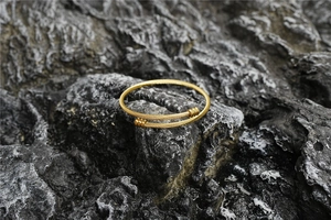 Détail d'un bracelet torsadé doré présenté sur une surface en pierre naturelle sombre