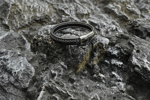 Detail eines schwarzen geflochtenen Lederarmbands für Herren mit weißen Nähten und Magnetverschluss
