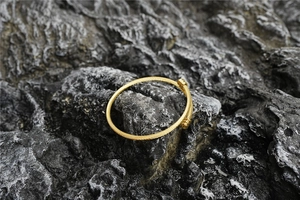 Bracelet jonc torsadé doré en gros plan sur un fond de roche volcanique gris foncé