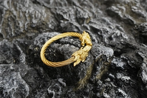 Détail d'un bracelet manchette doré à tête de dragon avec texture torsadée sur roche