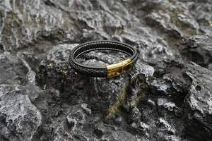 Detail eines gewebten schwarzen Lederarmbands mit goldener Magnetschließe auf Steinhintergrund