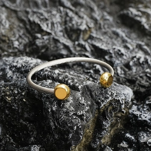 Bracelet torsadé minimaliste argenté avec embouts dorés sur un fond en pierre sombre