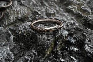 Detail of dark brown leather braided men's bracelet with silver metal clasp on rock