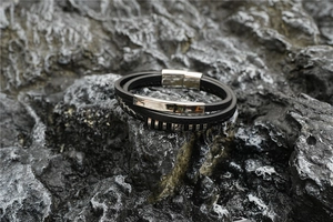 Détail du bracelet multicouche en cuir noir avec fermoir magnétique sur roche volcanique