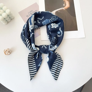 Close-up of silk square scarf tied in a bow with floral patterns and pearl chain motifs