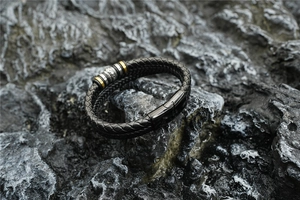 Détail du bracelet en cuir tressé noir avec anneaux gravés sur roche naturelle