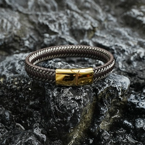 Men's woven leather bracelet with polished gold metal buckle on a dark rock background