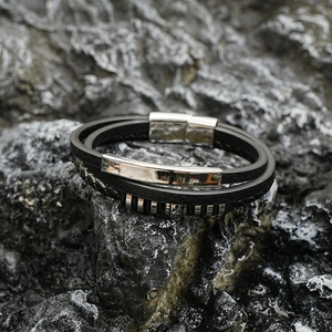 Bracelet multicouche en cuir noir avec insert en métal poli sur fond de roche sombre